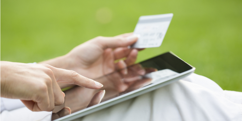 mão feminina segura um cartão de crédito e toca em um tablet com fundo verde indicando sazonalidade