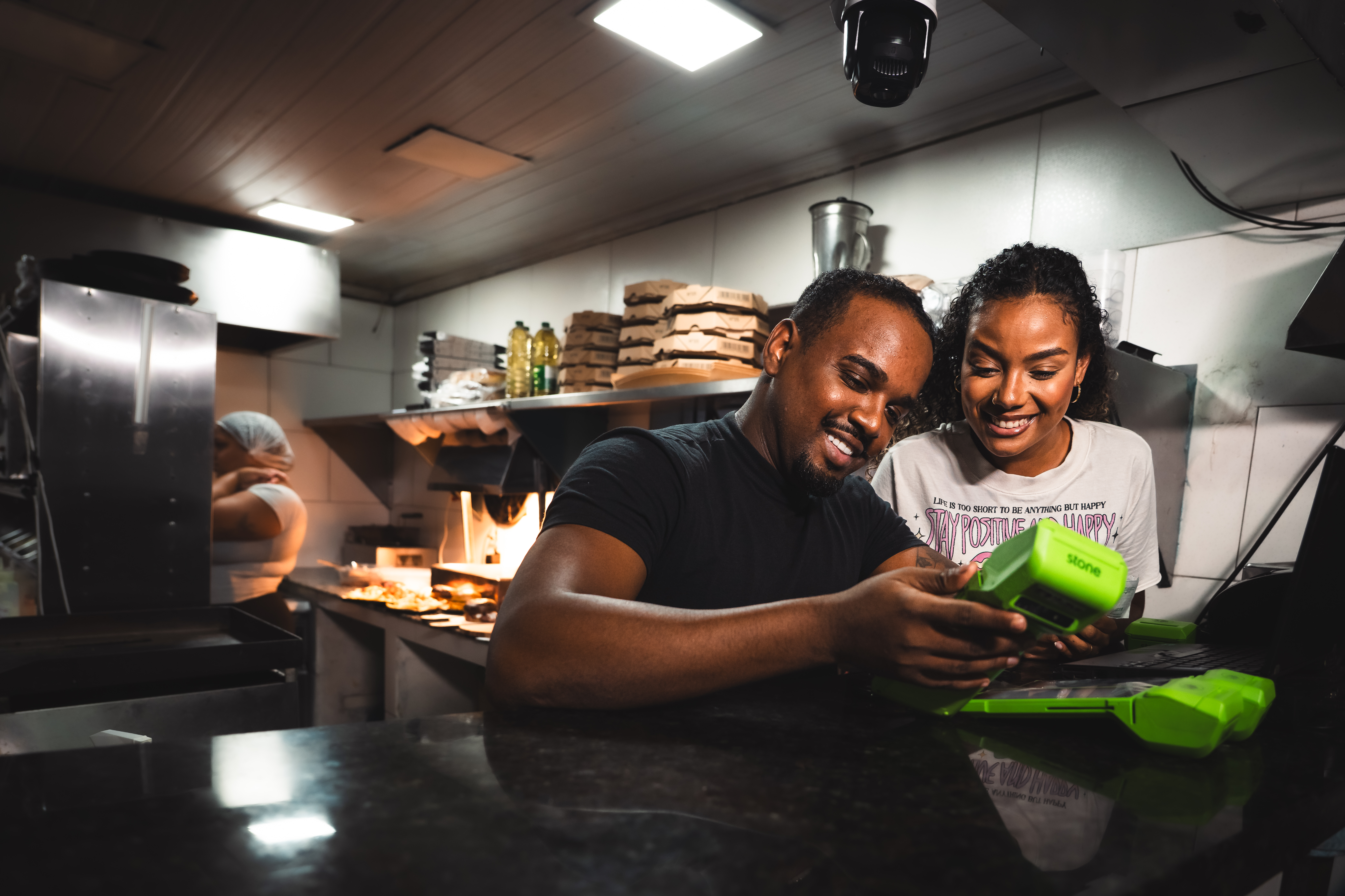 casal em cozinha de restaurante mexendo em uma maquininha stone