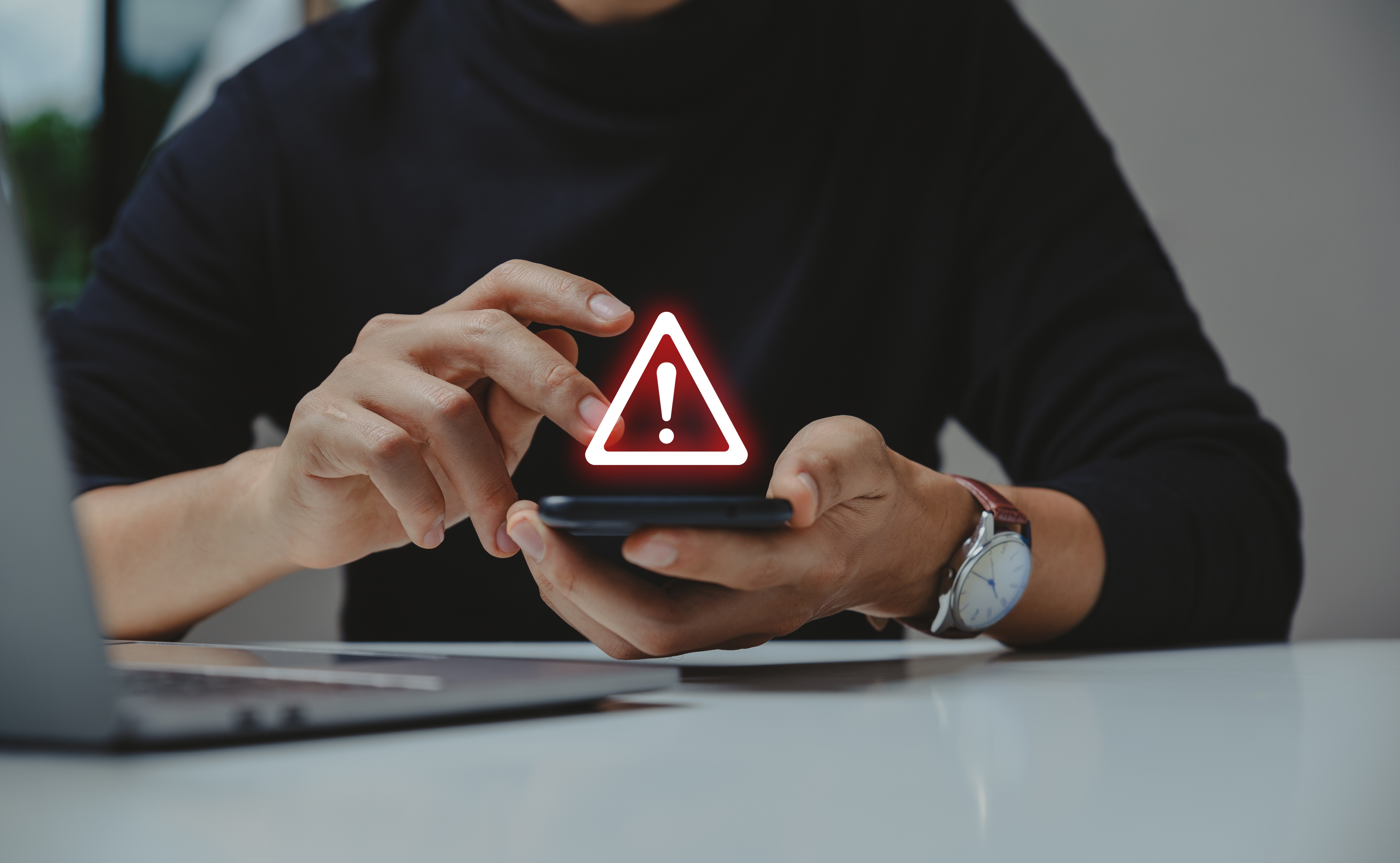 Homem mexendo no celular com um símbolo gráfico de atenção na frente