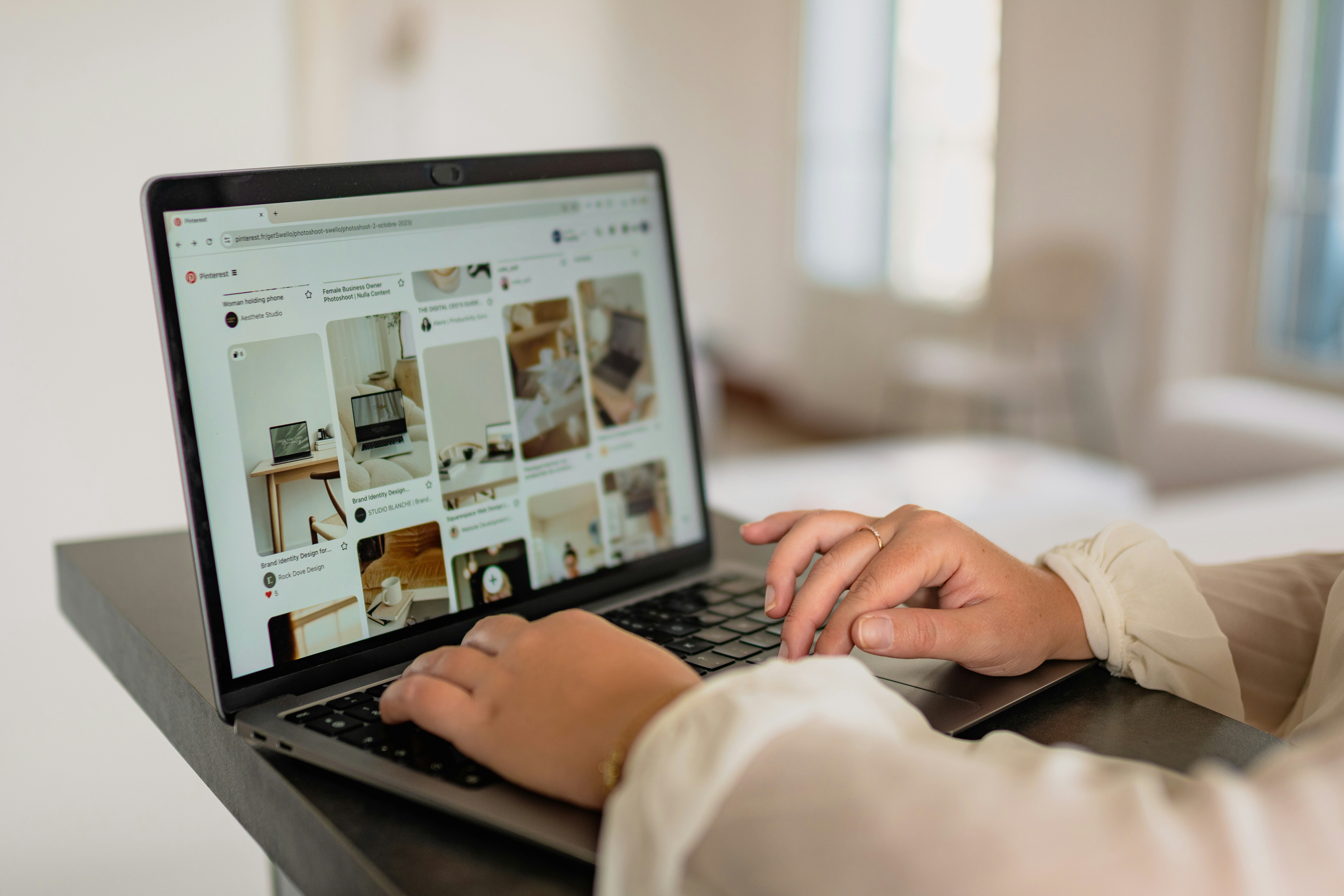 Na imagem, mãos femininas manuseiam um notebook aberto em uma tela do pinterest buscando referências ou produtos
