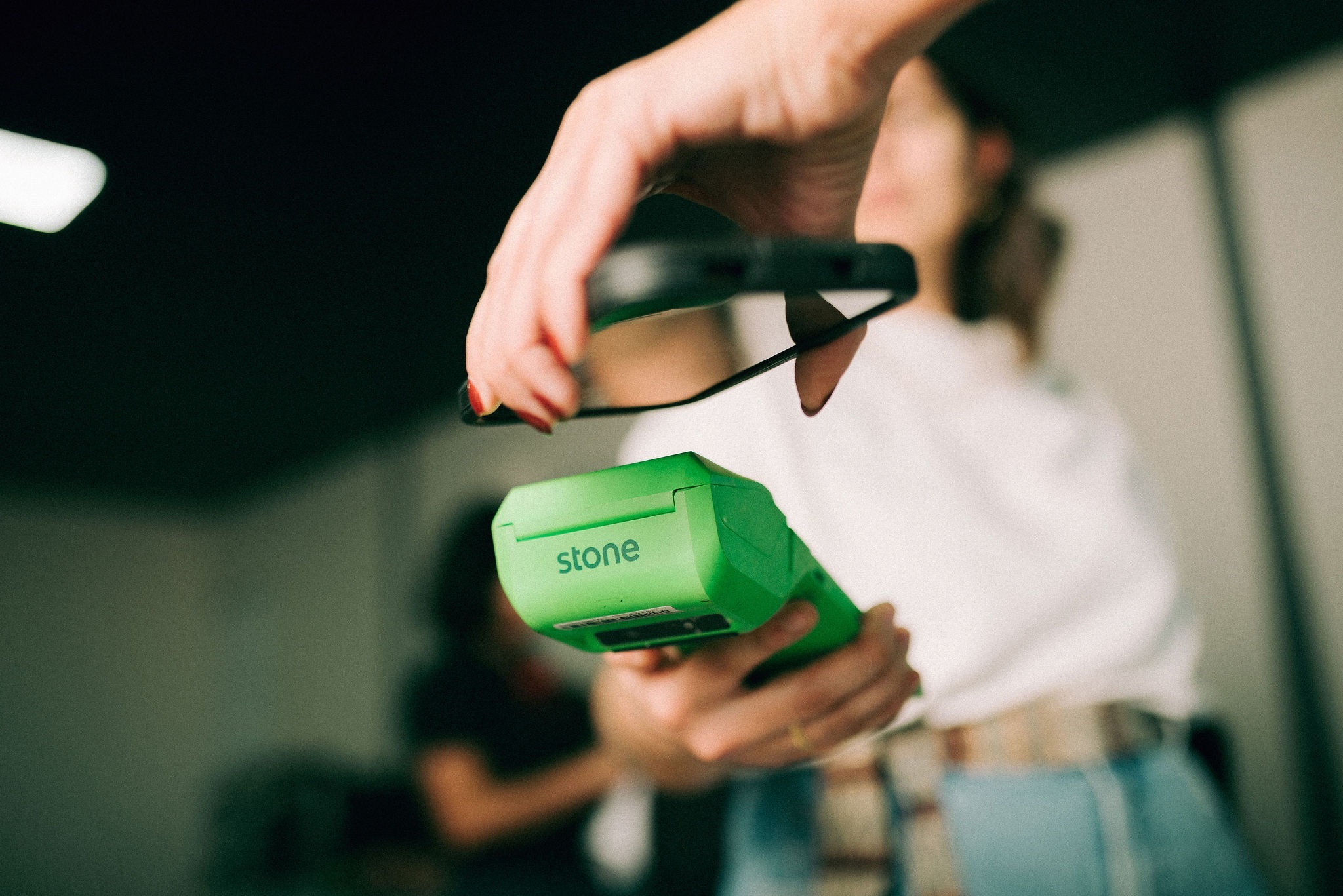 Mulher pagando com o celular por aproximação em Maquininha Stone