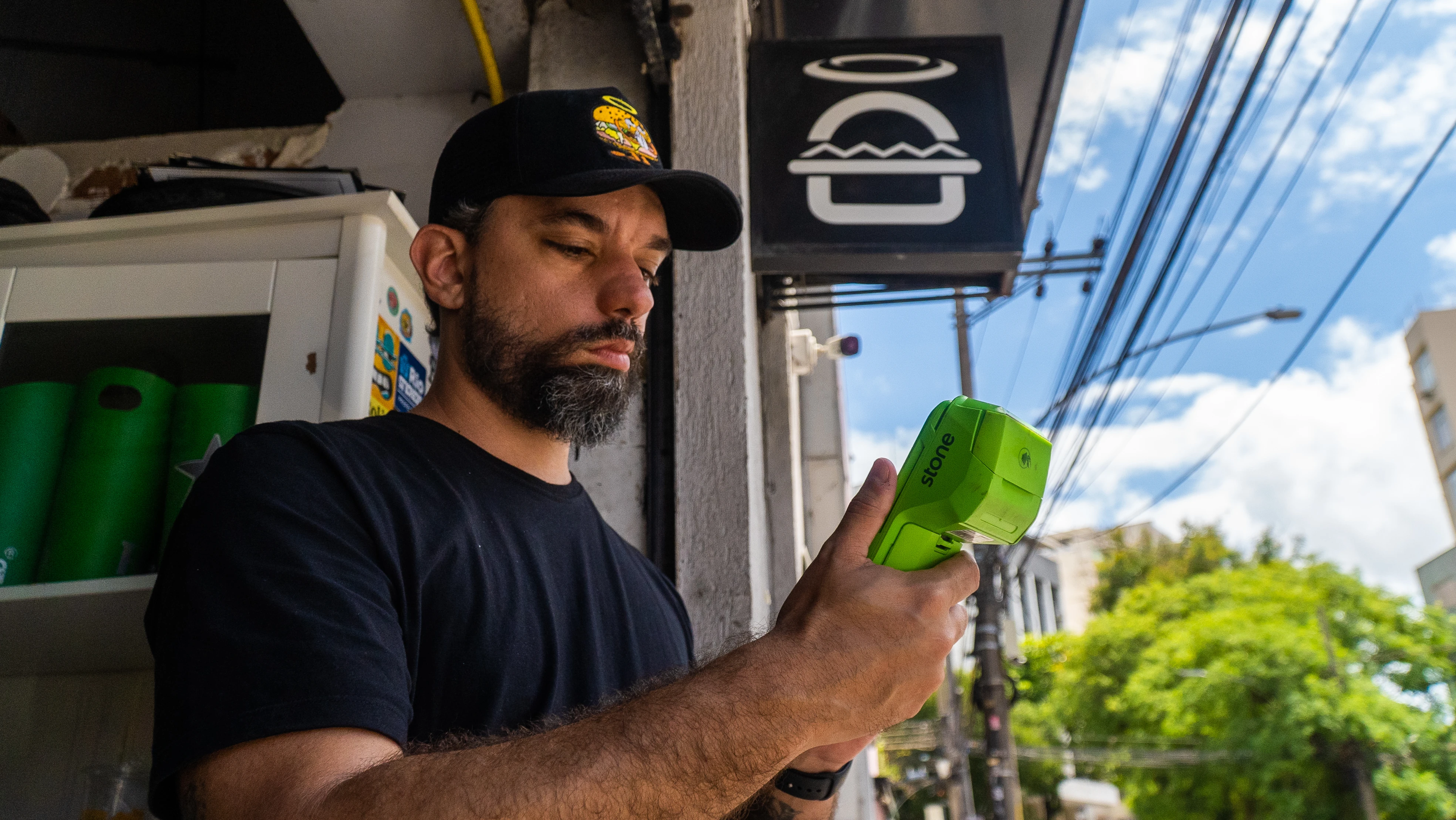 Sócio-proprietário do Encarnado Burger com maquininha Stone na frente da hamburgueria